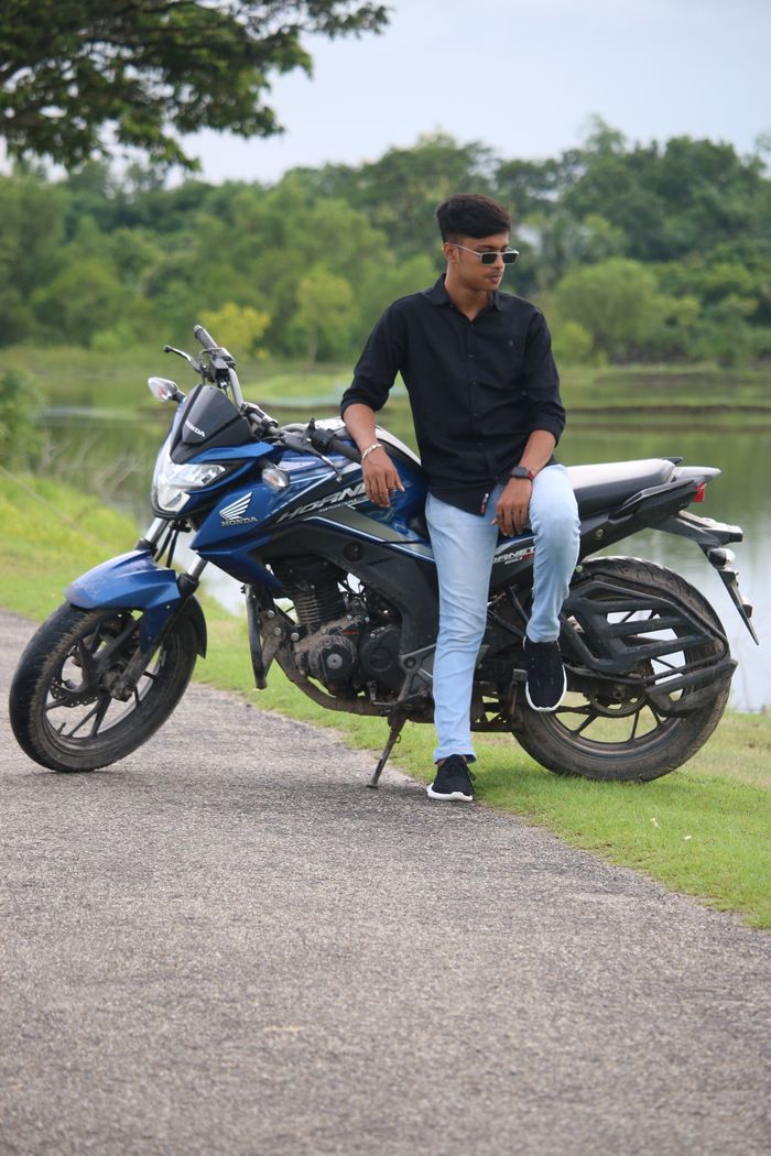 Man in sunglasses poses on a sports bike by a scenic area with trees and water.