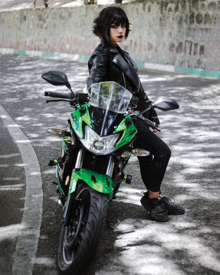 Stylish woman in black leather with motorbike on city street.