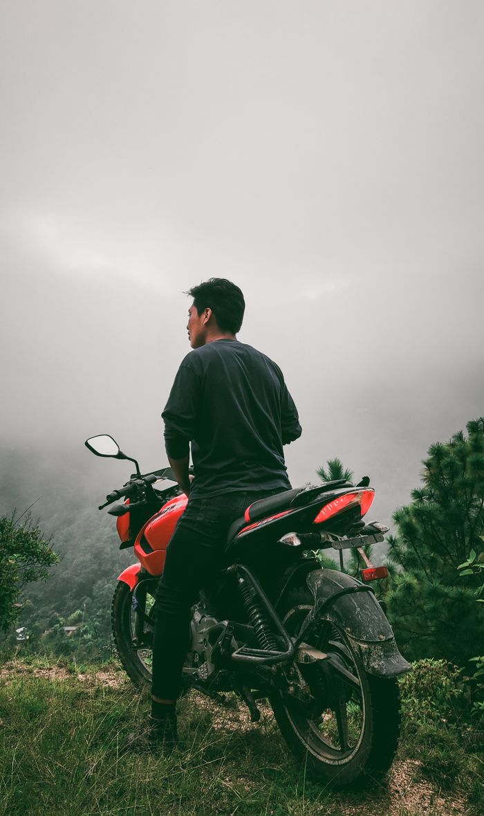 A man sitting on a motorcycle overlooking a misty and scenic rural landscape, perfect for adventure themes.