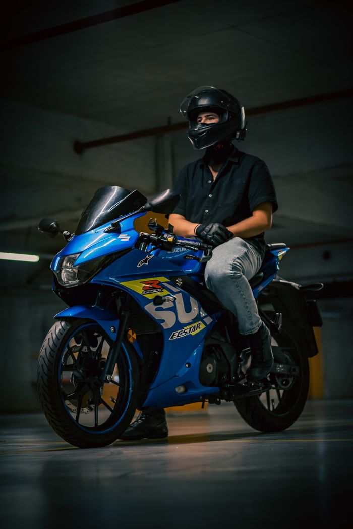 A person on a blue sport motorcycle in a dimly lit underground parking area.