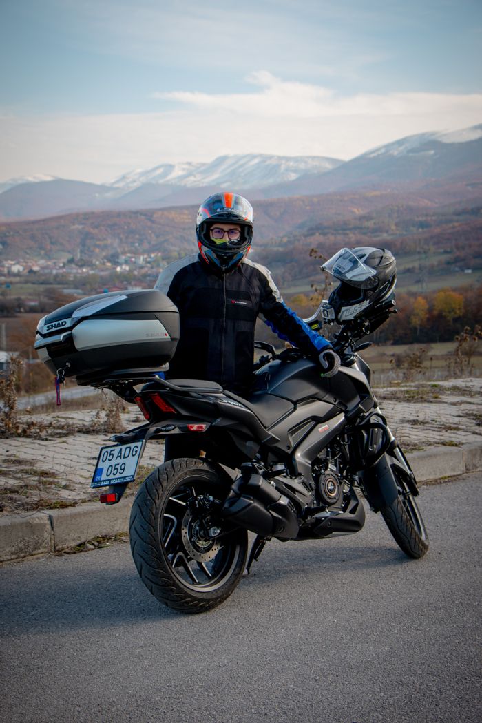 A motorcyclist poses on a mountain road in Amasya, Turkey, with autumn scenery.