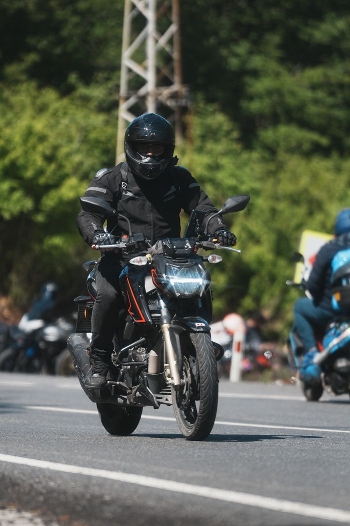 A motorcyclist in full gear rides his bike on a road, captured on a sunny day.