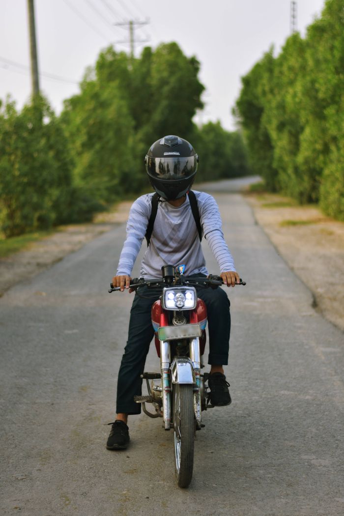 Person on a motorcycle drives down a rural road surrounded by lush greenery.